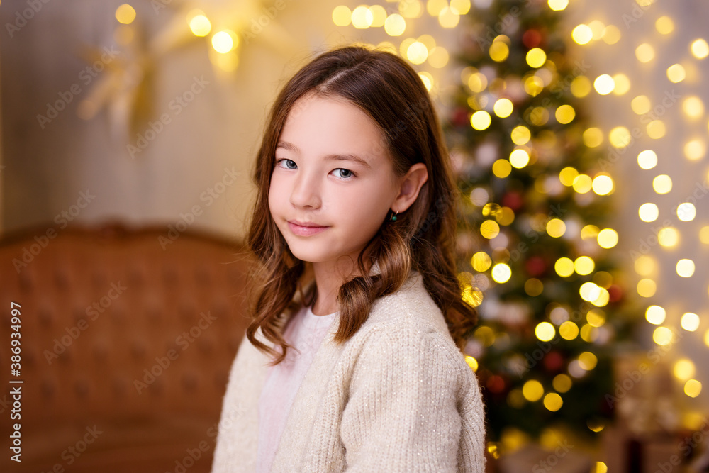 Christmas and childhood concept - close up portrait of cute little girl posing in decorated living room with Christmas tree and lights Christmas and childhood concept - close up portrait of cute little girl posing in decorated living room with Christmas tree and lights