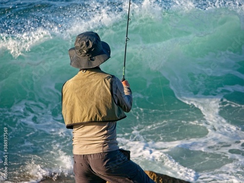 Pescador de espaldas echando el anzuelo contra las olas