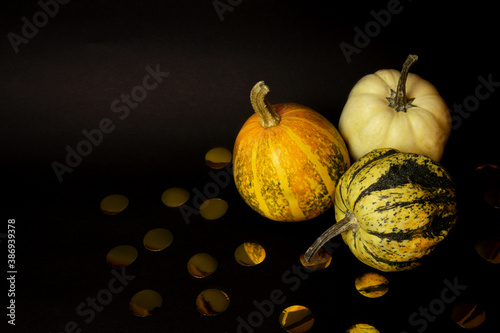 Three pumpkins and decor from paper gold confetti isolated on a black background. It's Halloween time. Halloween mood. Minimal creative stillife