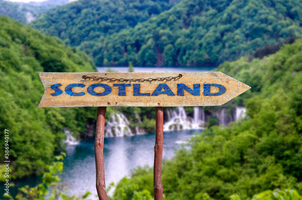 Scotland wooden arrow road sign against waterfall, mountain river and forest view. Travel to Scotland concept.