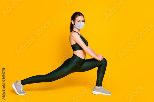 Photo of sportive young lady stretching sit one leg wear mask sports suit top pants sneakers isolated yellow color background
