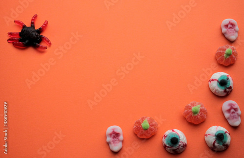 Halloween. Jelly candies in the form of huge black spider, orange pumpkins, skulls, eyes and brains on an orange background. Copy space