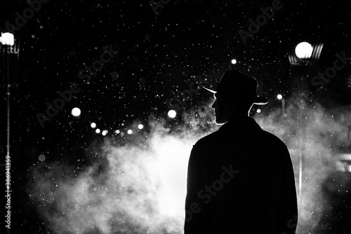 Schilderij op canvas dark silhouette of a man in a hat in the rain on a night street in a city