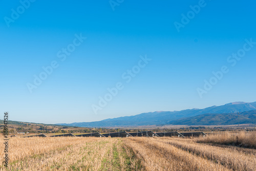 Person view yellow agricultural fields harvest next to solar panel station picturesque countryside rural area bulgaria mountains tech sheaves bails of hay scattered on field