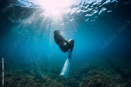 Free diver woman with white fins glides underwater with amazing sun rays. Freediving underwater in sea