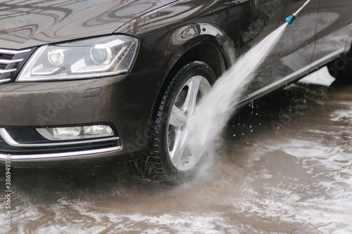 Car washing. Cleaning car using high pressure water. Man washing his car outdoor. Close-up