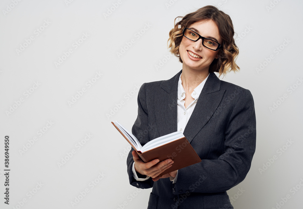 A woman in a jacket with a book in her hands on a light background glasses on her face with curly hair A woman in a jacket with a book in her hands on a light background glasses on her face with curly hair