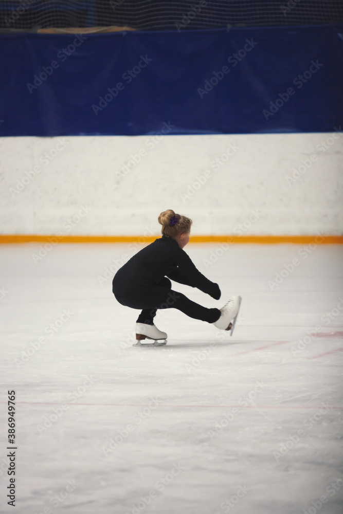 Figure skating school. Young figure skater practicing sit spin at indoor skating rink. Kid learning to ice skate. Figure skating school. Young figure skater practicing sit spin at indoor skating rink. Kid learning to ice skate.