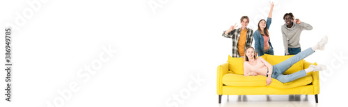 Panoramic shot of cheerful multiethnic teenagers showing peace sign near yellow couch on white background