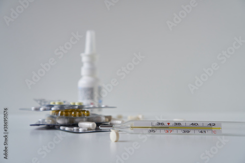 Assorted pharmaceutical medicine pills, tablets and capsules, nasal spray, thermometer.