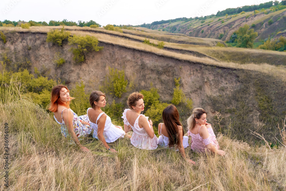 A cheerful company of beautiful girls friends enjoy a picturesque panorama of the green hills at sunset