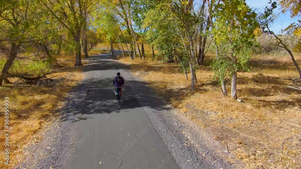 Elderly man cycling along a nature tail in autumn - aerial follow view Elderly man cycling along a nature tail in autumn - aerial follow view
