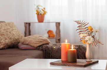 burning candles with autumn decor on white table at home