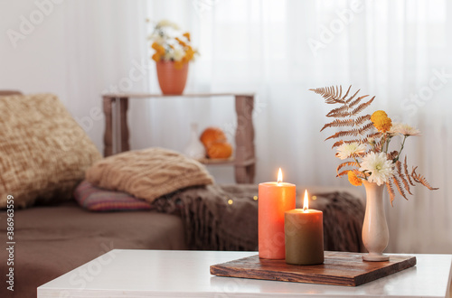 burning candles with autumn decor on white table at home