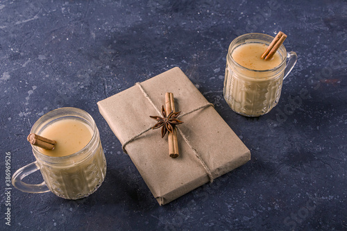 Traditional American and Kandacian Christmas drink eggnog in crystal glasses with cinnamon or nutmeg. Gift box for the New Year decorated with cinnamon stick and anise star. Winter holidays, backlight photo