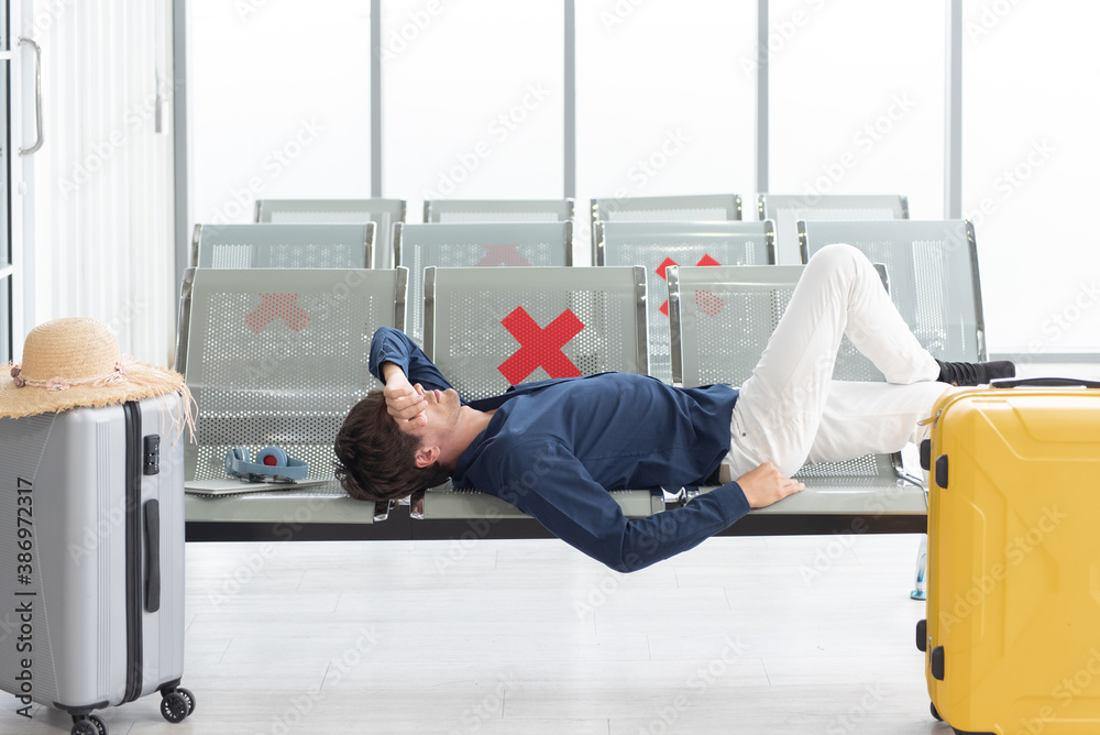 Tired caucasian tourists lying on a chair at the airport with his baggage
