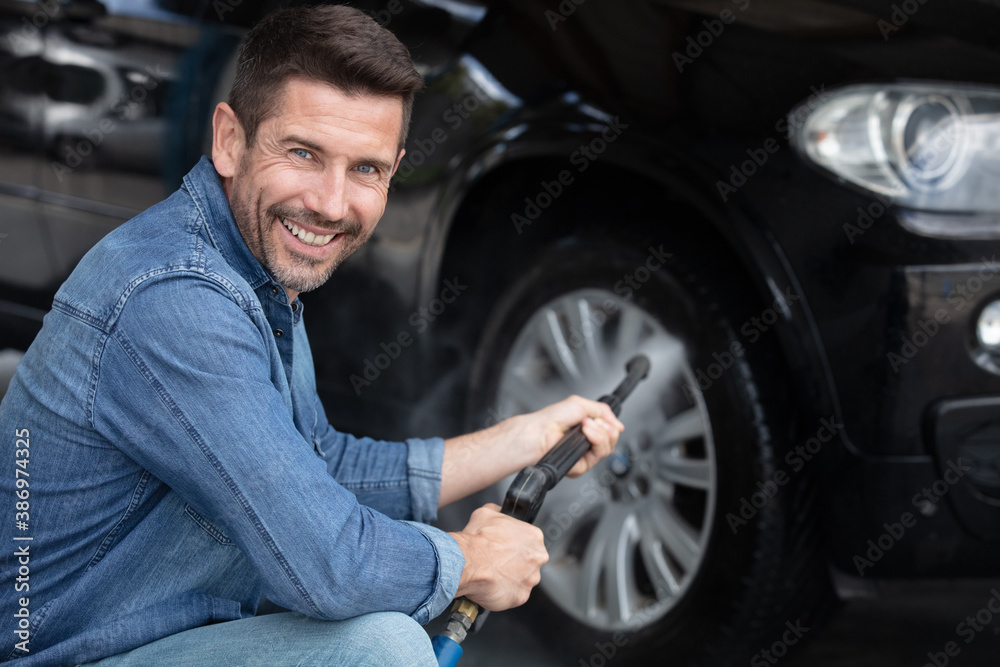 man washes a wheel from a hose with high-pressure water