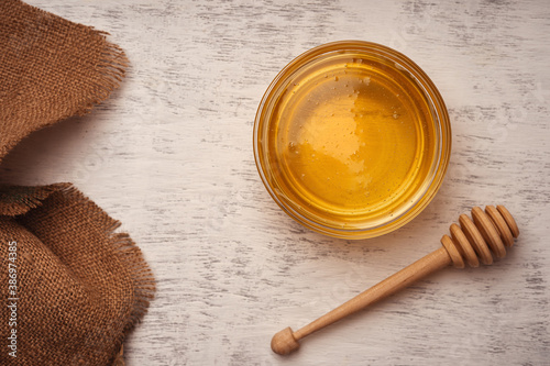 Fresh acacia honey in a glass bowl near a wooden spoon for honey and burlap  top view