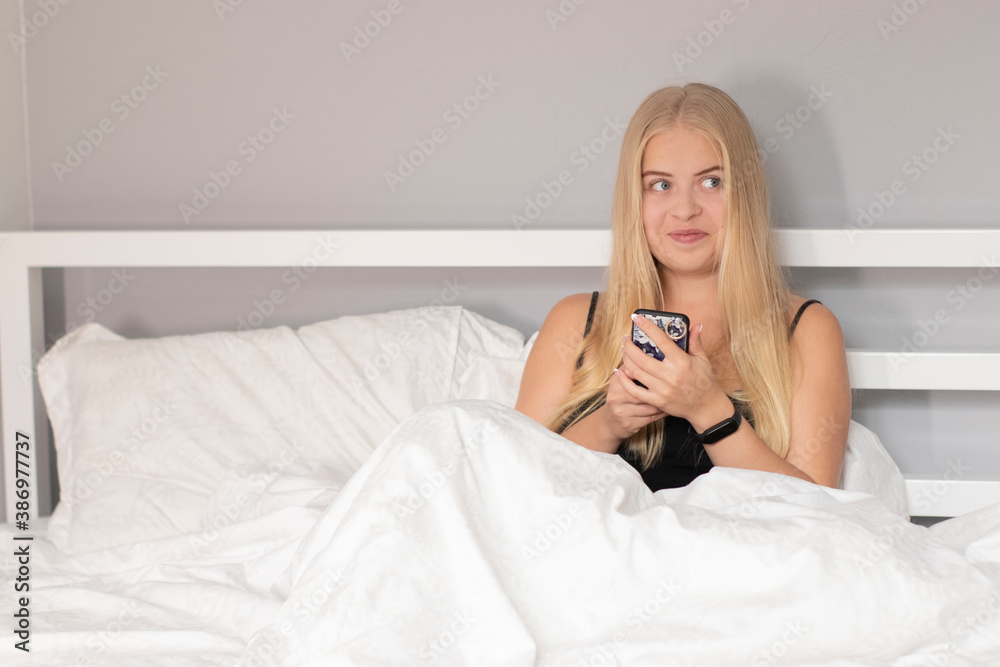 pensive thoughtful blonde on white bed with phone. pretty people on isolation. pensive thoughtful blonde on white bed with phone. pretty people on isolation.