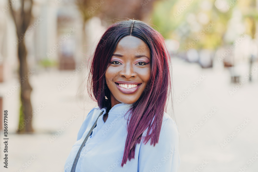 a smiling young African American girl with pink hair and a blue shirt walking outside on a sunny day. a smiling young African American girl with pink hair and a blue shirt walking outside on a sunny day.