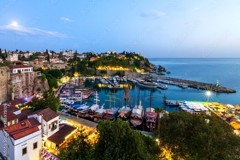 Panorama of the old city in Antalya, the old port in the harbor are yachts and ships, evening illumination of the city