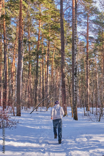 A man runs on a snowy road in a mixed forest on a sunny day.
