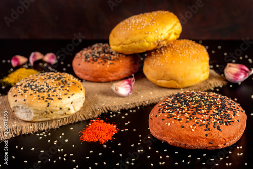 
Spiced garlic beet burger buns with poir seeds on top on black table and photo