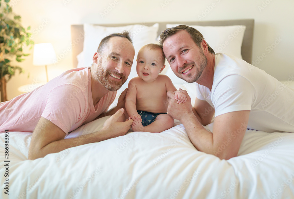 Male gay parents relaxing in bed with baby Male gay parents relaxing in bed with baby