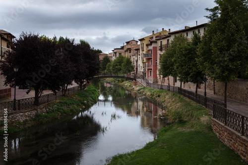 City landscape of the medieval village of Molina de Aragón with colorful houses overlooking the river and a wooden bridge crossing it on a cloudy day, Guadalajara, Spain