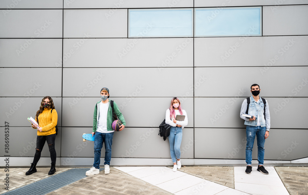 Obraz premium Young students with face mask in casual clothes standing in front of a grey wall background - New normal concept with people going to school