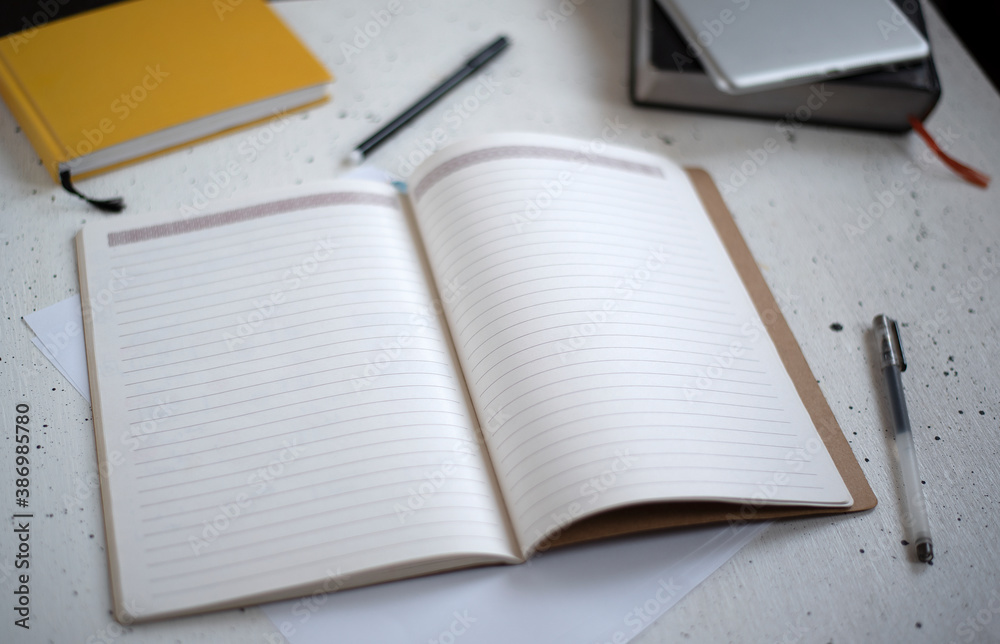An open notebook with blank pages and a black pen on a light background. Diary, book, and tablet in the background. Top view. Space for text. Flat lay workspace and planning. An open notebook with blank pages and a black pen on a light background. Diary, book, and tablet in the background. Top view. Space for text. Flat lay workspace and planning.