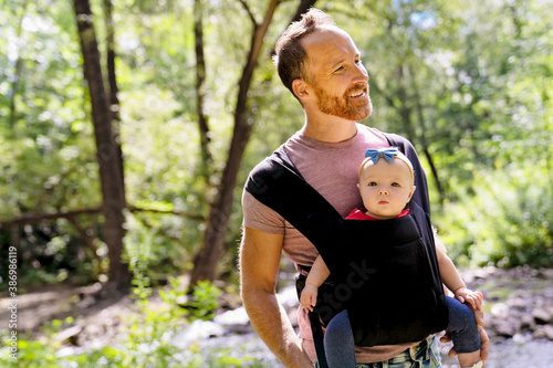 beautiful caring father holding her baby child in a sling walking on nature