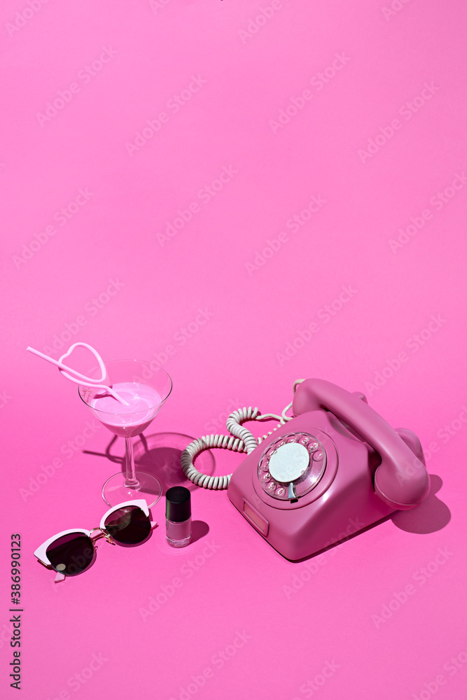 Fototapeta premium Retro concept stage made with rotary telephone, nail polish and sunglasses on vibrant pink table background. Minimal art direction. Vintage 70s aesthetic trend shadows.