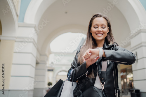 looking at the watch on her hand, a woman of Caucasian appearance, a brunette in a black leather jacket, is in a good mood.