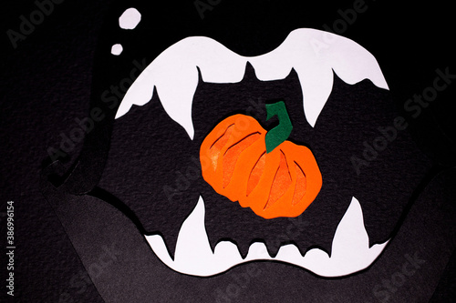 Black lips with white fangs cut out of paper with orange pumpkin inside on a black background. The photo of paper art was shot close-up for your craft Halloween design. photo