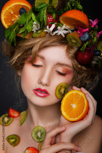 Beaty shooting a beautiful girl with kiwi, oranges, lime and flowers on a black background in the studio