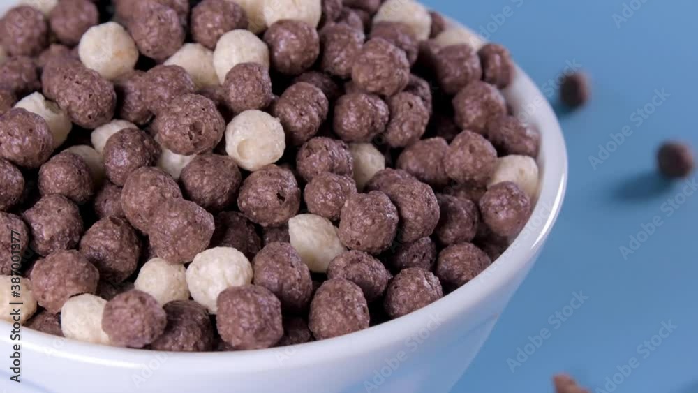 Chocolate Flakes. Chocolate cereal flakes for breakfast poured into a bowl on blue background. Healthy breakfast. Flakes pour into a plate.