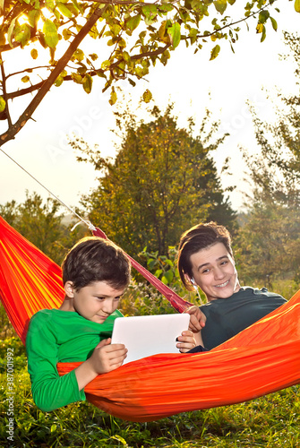 Two boys in orange hammocks on a green background. Children play with laptop and tablet. The concept of online learning in nature.