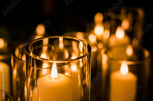 Romantic wedding display of wax candles glowing with small flames in glass vases centrepieces