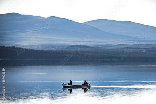 Two people canoing over a clear, calm and stunning lake surrounded by mountains and wilderness in Northern Canada. 