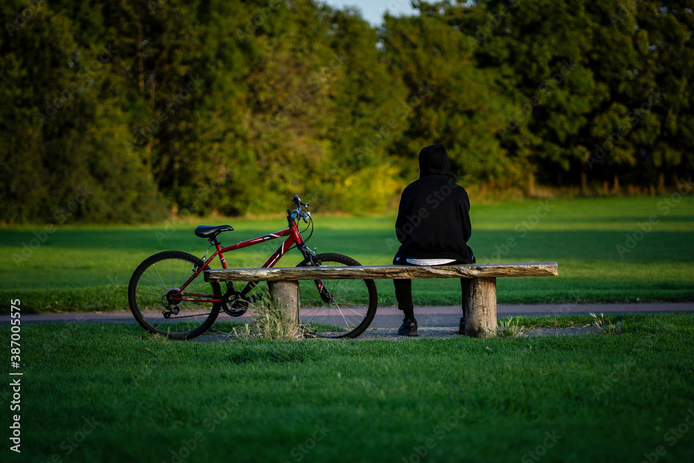 Obraz premium Person sitting on bench with his bicycle beside him