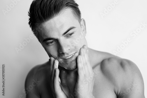 Muscular sexy model sports young man. Black and white portrait of beautiful smiling healthy guy applying foam for washing on his face. Facial skincare routine.