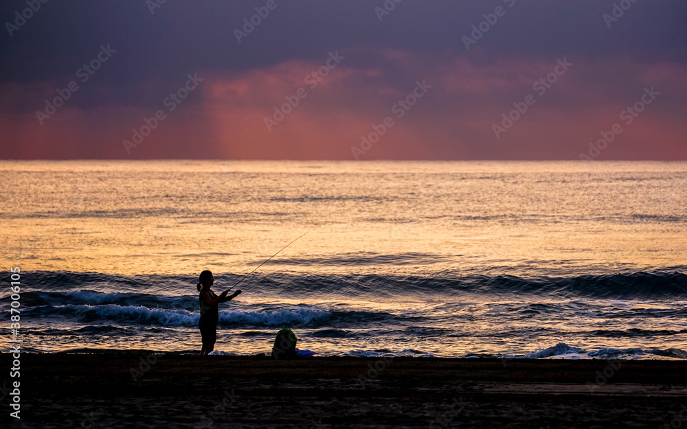 woman fishing in the sea at sunrise