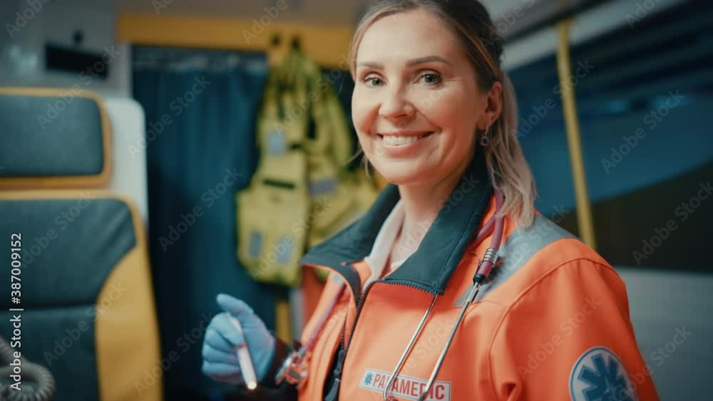 Calm and Happy Female EMS Professional Paramedic Smiles on Camera in Ambulance Vehicle. Successful Emergency Medical Technician on Their Way to a Call Outside the Healthcare Hospital.