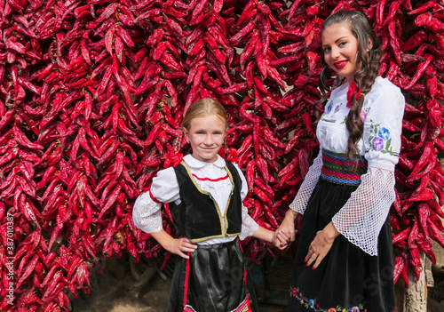 Girls dressed on traditional Serbian Balkan clothing  national folk costume. Posing near of lot red paprika peppers.