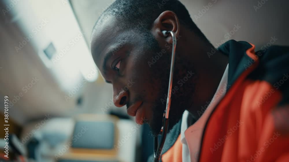 Close up handheld footage of a black professional paramedic providing medical help to an injured patient on the way to hospital