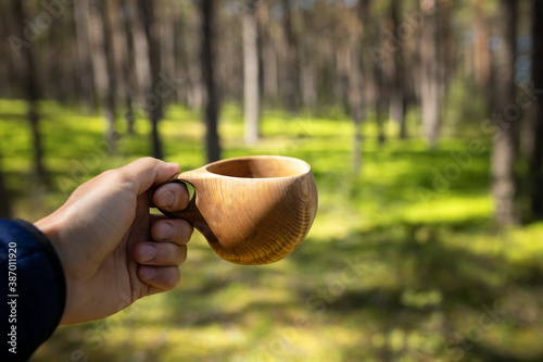 Man hand with cup of coffee. Camping wooden mug with a warm drink. Concept of camping in the forest photo