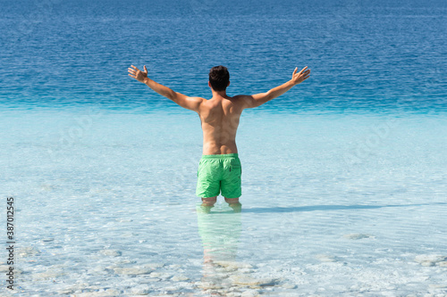 Back view of young caucasian man enjoying crystal water and sunbathing
