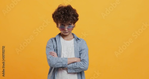 Grumpy little boy in sunglasses getting offended, standing with folded hands and looking sullenly