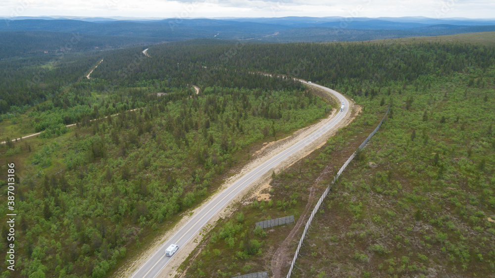 Scenic asphalt road with cars through the beautiful view of hills in Lapland during summer. Concept of roadtrip, travel, vacation, adventure.